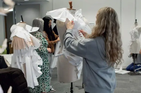 A student arranges and styles a paper outfit onto a mannequin