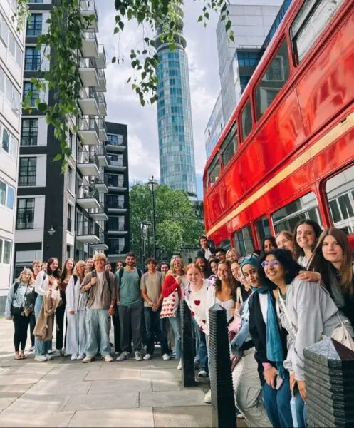 Students standing by a red London bus on the first day of the summer school
