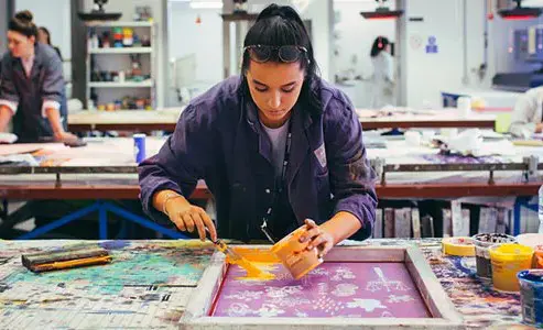 Student using paint and in the process of printmaking in an art studio